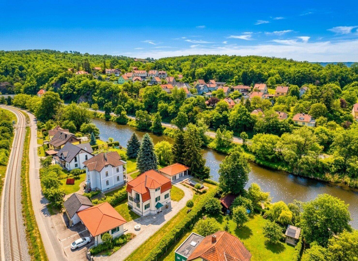 Luftaufnahme der Wohngegend mit Fluss, Eisenbahnlinie und grüner Hügellandschaft.