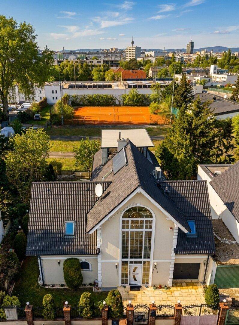 Luftaufnahme eines eleganten Hauses mit Satteldach und Blick auf die Stadt und einen Tennisplatz.