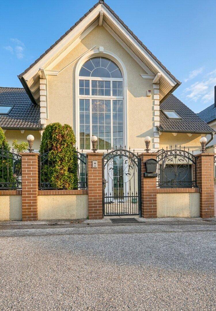 Repräsentative Hausfassade mit großem Bogenfenster und schmiedeeisernem Tor, umgeben von Ziegelpfeilern.
