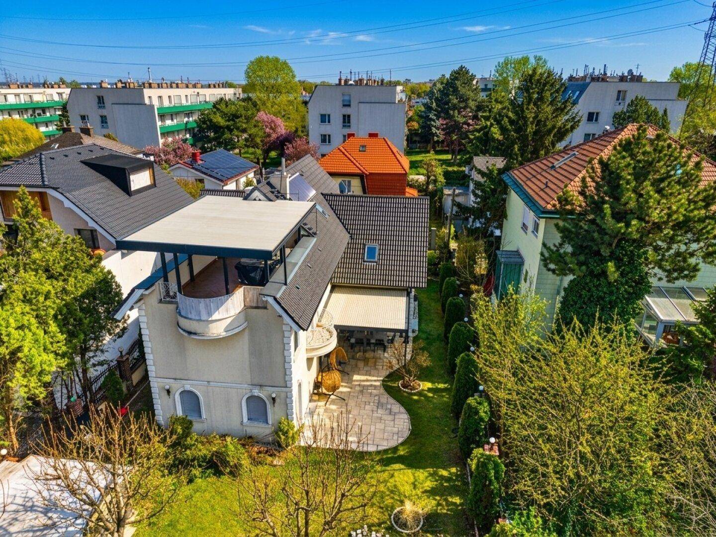 Luftaufnahme eines modernen Einfamilienhauses mit Garten, Terrasse und umliegender Wohnbebauung.