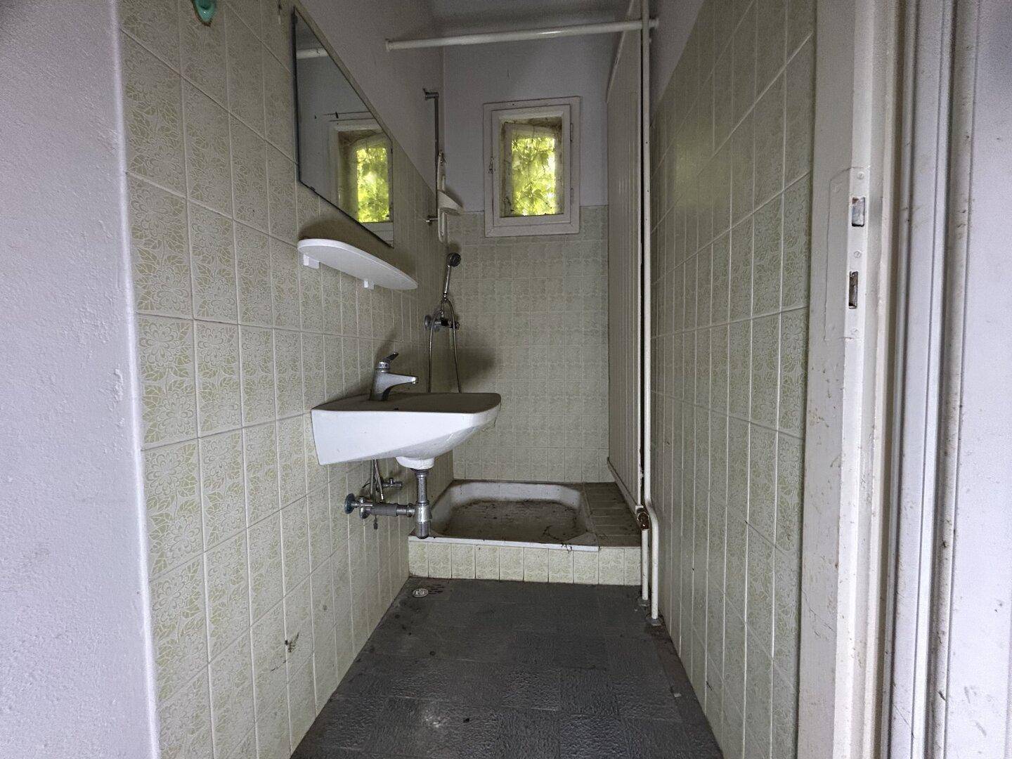 Sehr einfaches Badezimmer mit Hocktoilette, Waschbecken und Duschkopf, die Fliesen sind alt.