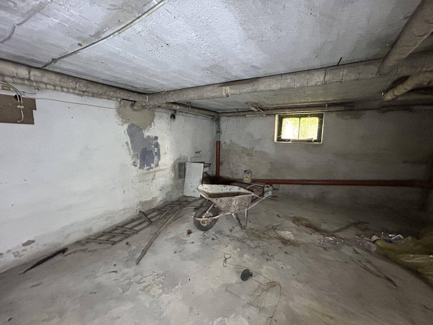 Rohbau-Kellerraum mit Betonboden, sichtbaren Leitungen und einem kleinen Fenster, bereit für die Renovierung.