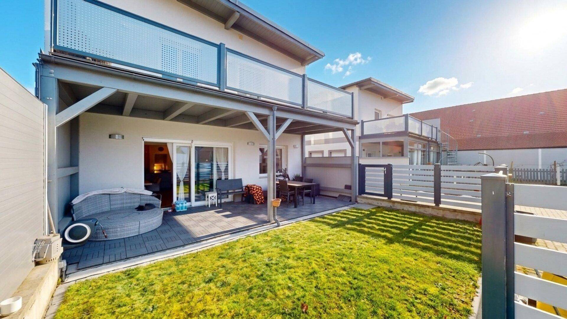 Gepflegter Gartenbereich mit Terrasse und Rasenfläche, umgeben von einem modernen Zaun.
