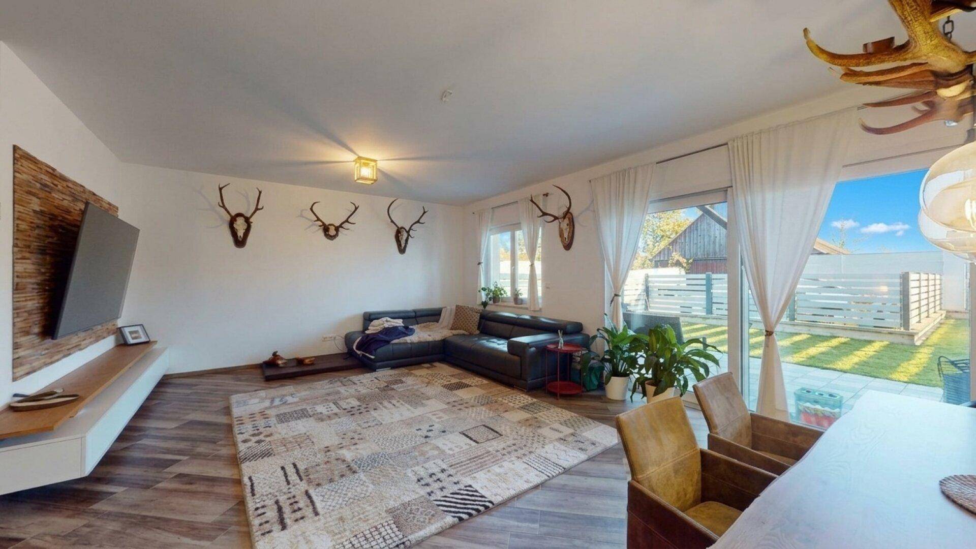 Gemütliches Wohnzimmer mit großem Sofa, Holzboden und Zugang zum Gartenbereich.