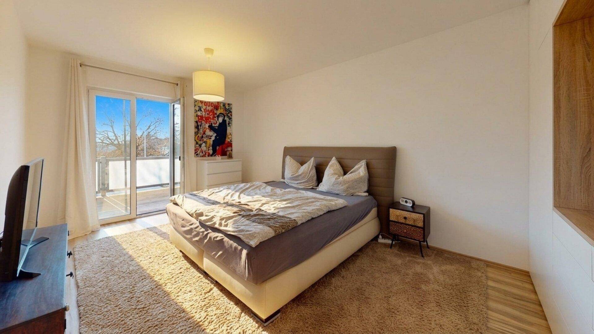 Helles Schlafzimmer mit Doppelbett, Teppichboden und direktem Zugang zum Balkon.