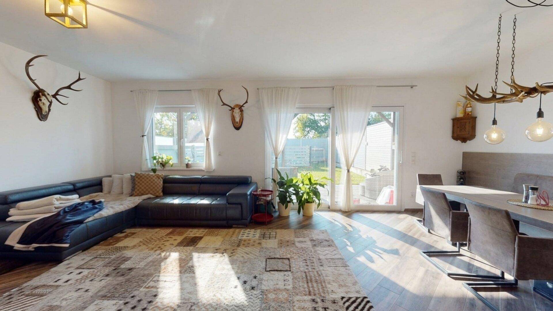 Lichtdurchfluteter Wohn- und Essbereich mit großem Sofa und Zugang zum Garten.