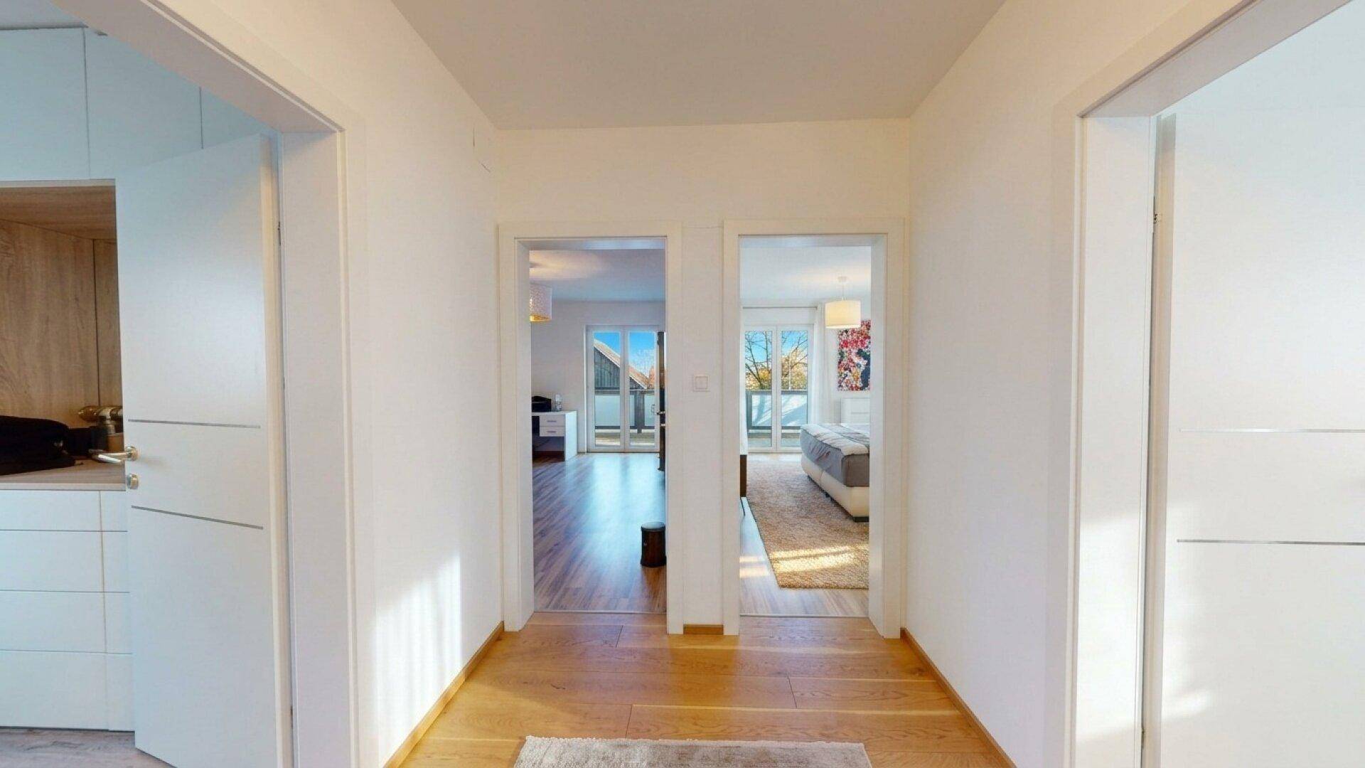 Heller Flur mit Holzboden und Zugang zu mehreren Zimmern, darunter Schlafzimmer und Wohnbereich.