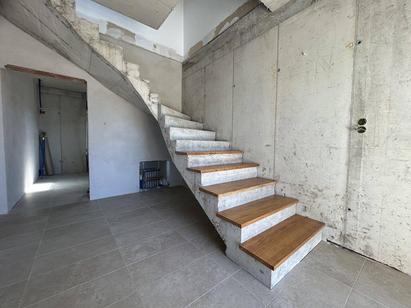 Rohbau-Treppenhaus mit Betonwänden, gefliestem Boden und Holzstufen, bereit für den weiteren Ausbau.