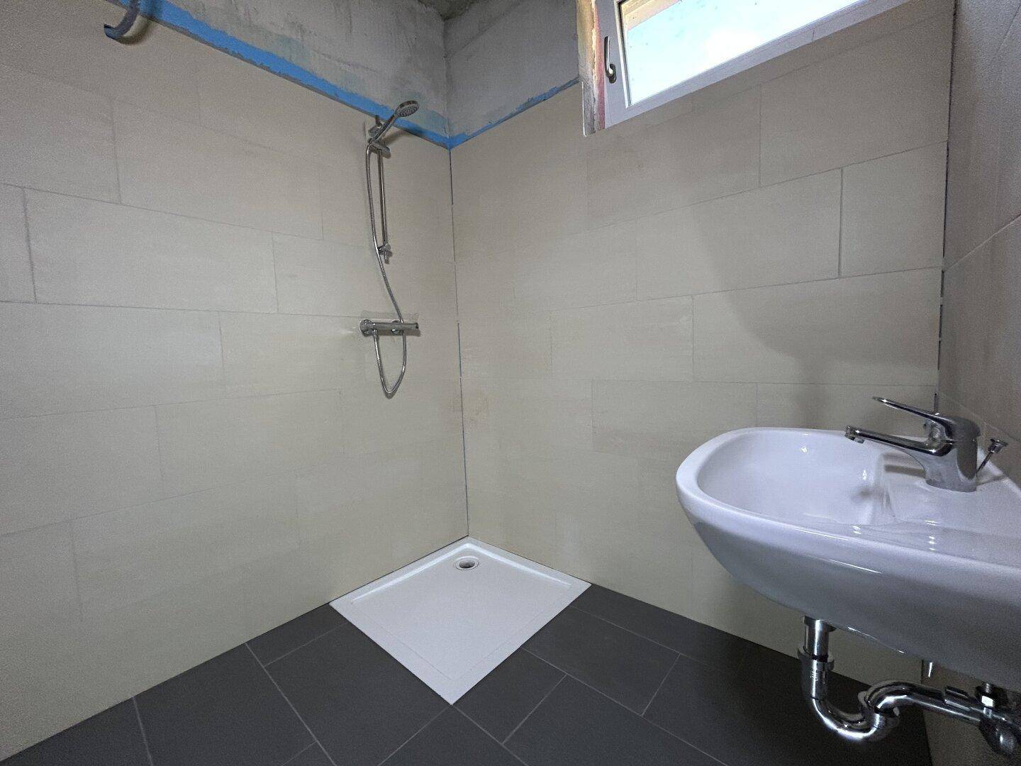 Modernes Badezimmer mit Duschbereich, Waschbecken und Fenster, hell und dunkel gefliest.