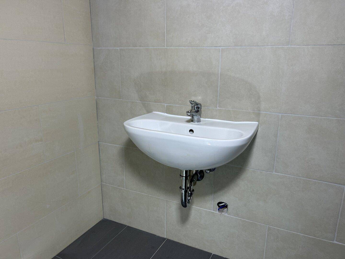Wandhängendes Waschbecken in einem modern gefliesten Raum mit hellen Wand- und dunklen Bodenfliesen.