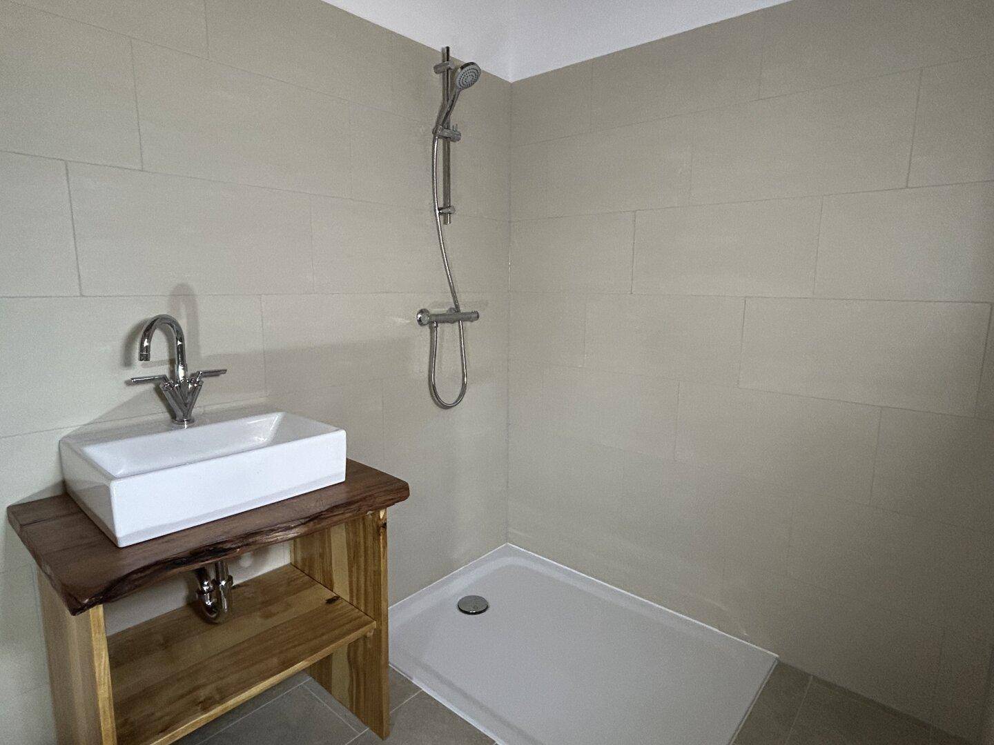 Modernes Badezimmer im Rohbau mit Duschbereich, Waschbecken und hellen Fliesen.