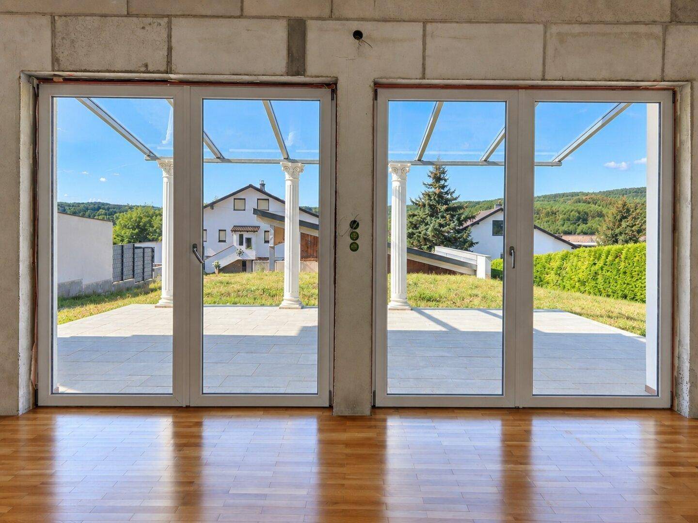 Blick durch große Glastüren auf die überdachte Terrasse und die umliegende Landschaft.