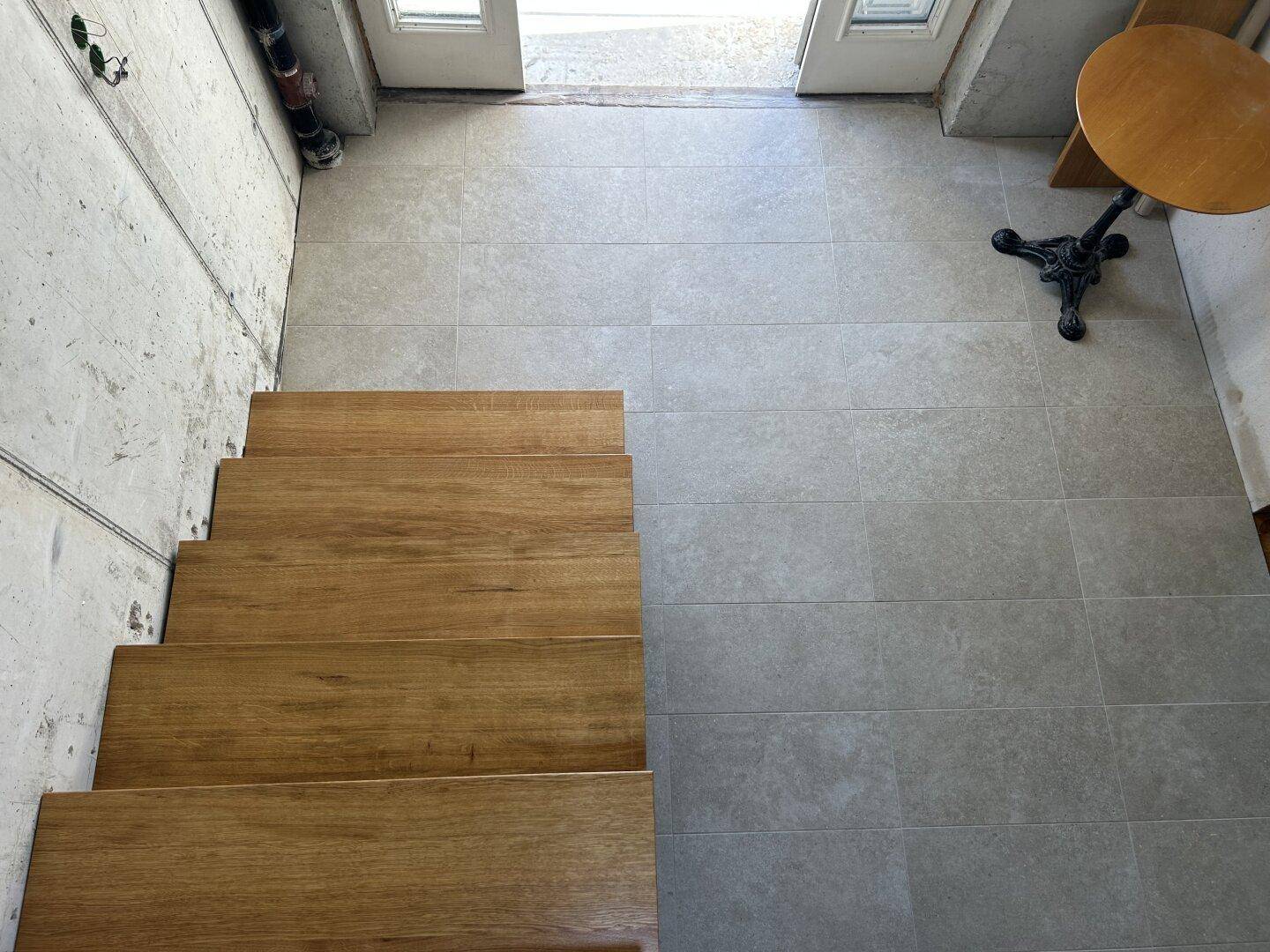 Gefliester Eingangsbereich mit Holztreppe und Ausgang ins Freie, ein kleiner Tisch steht bereit.