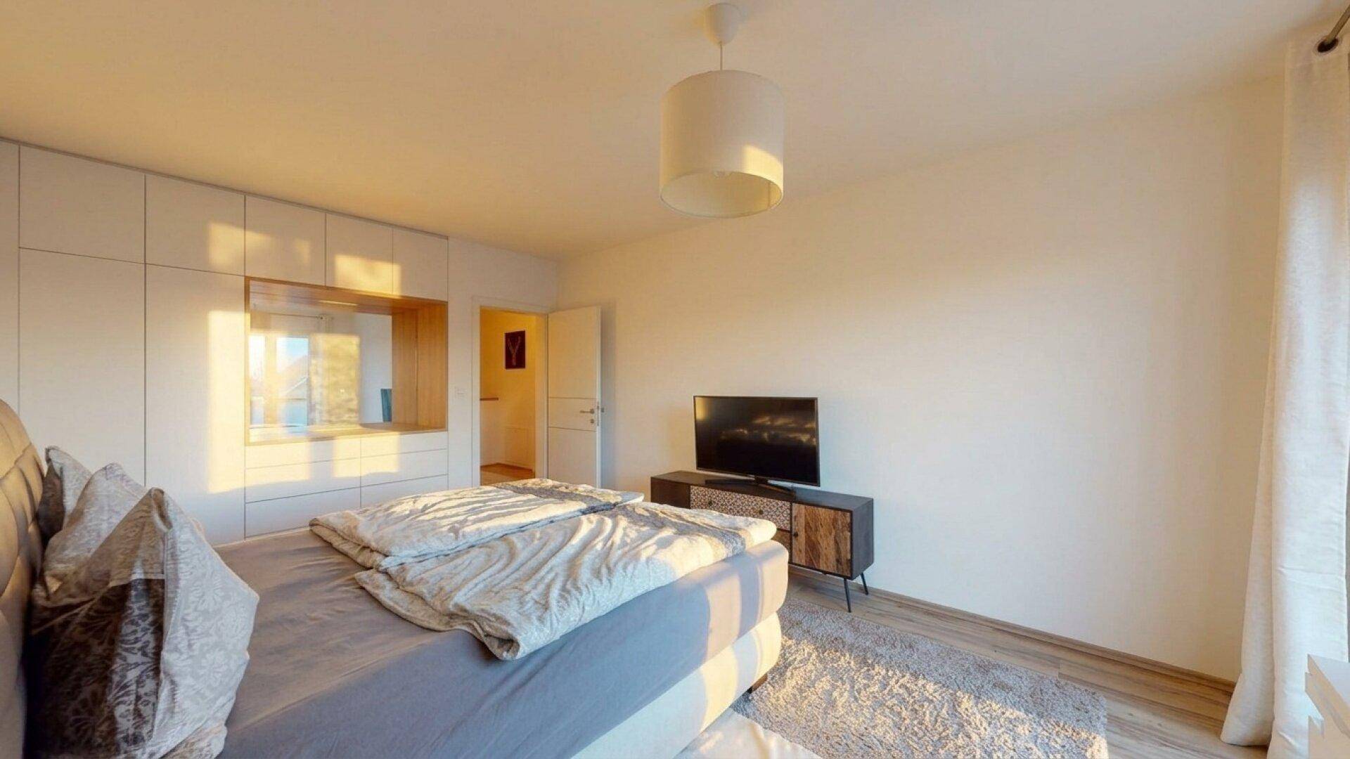 Gemütliches Schlafzimmer mit Doppelbett, Einbauschränken und viel natürlichem Licht am Abend.