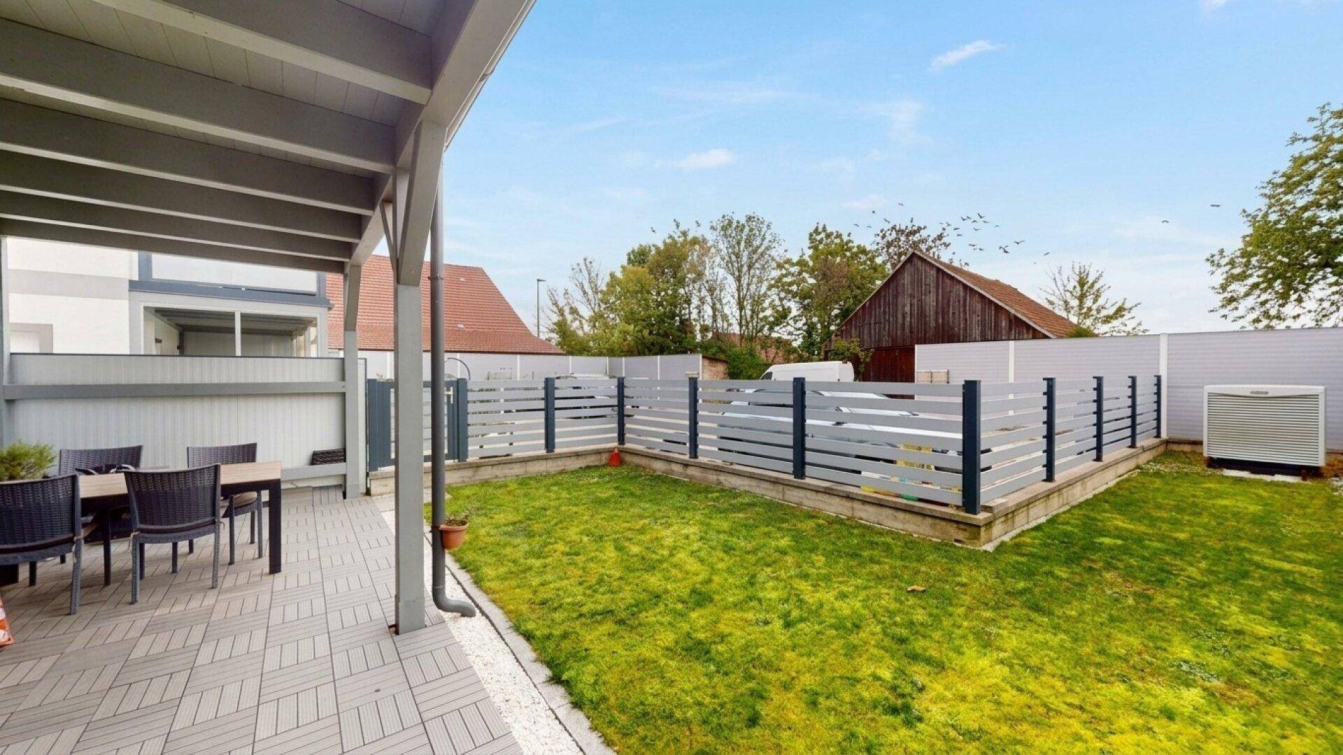 Gepflegter Gartenbereich mit Rasenfläche und überdachter Terrasse, ideal für Entspannung im Freien.