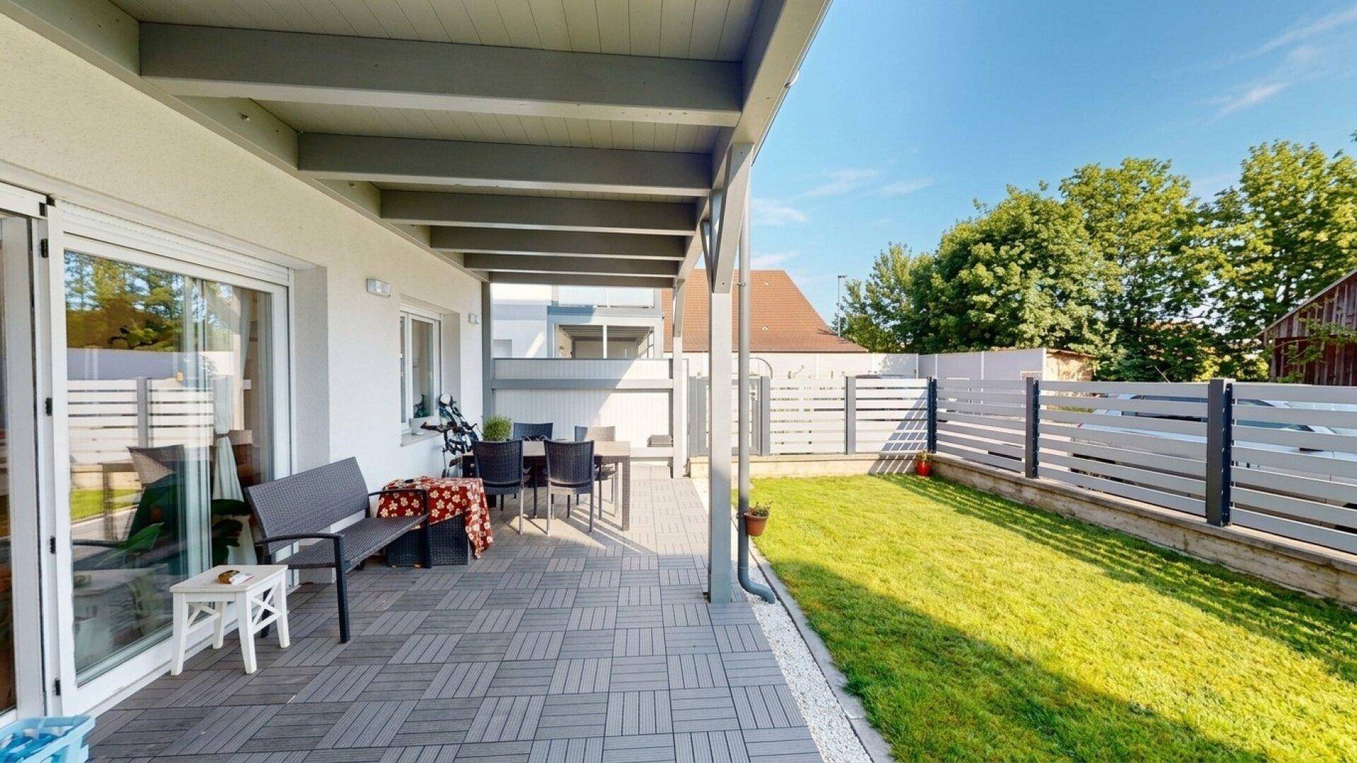 Überdachte Terrasse mit Essbereich und Zugang zum Garten, umgeben von einem modernen Zaun.