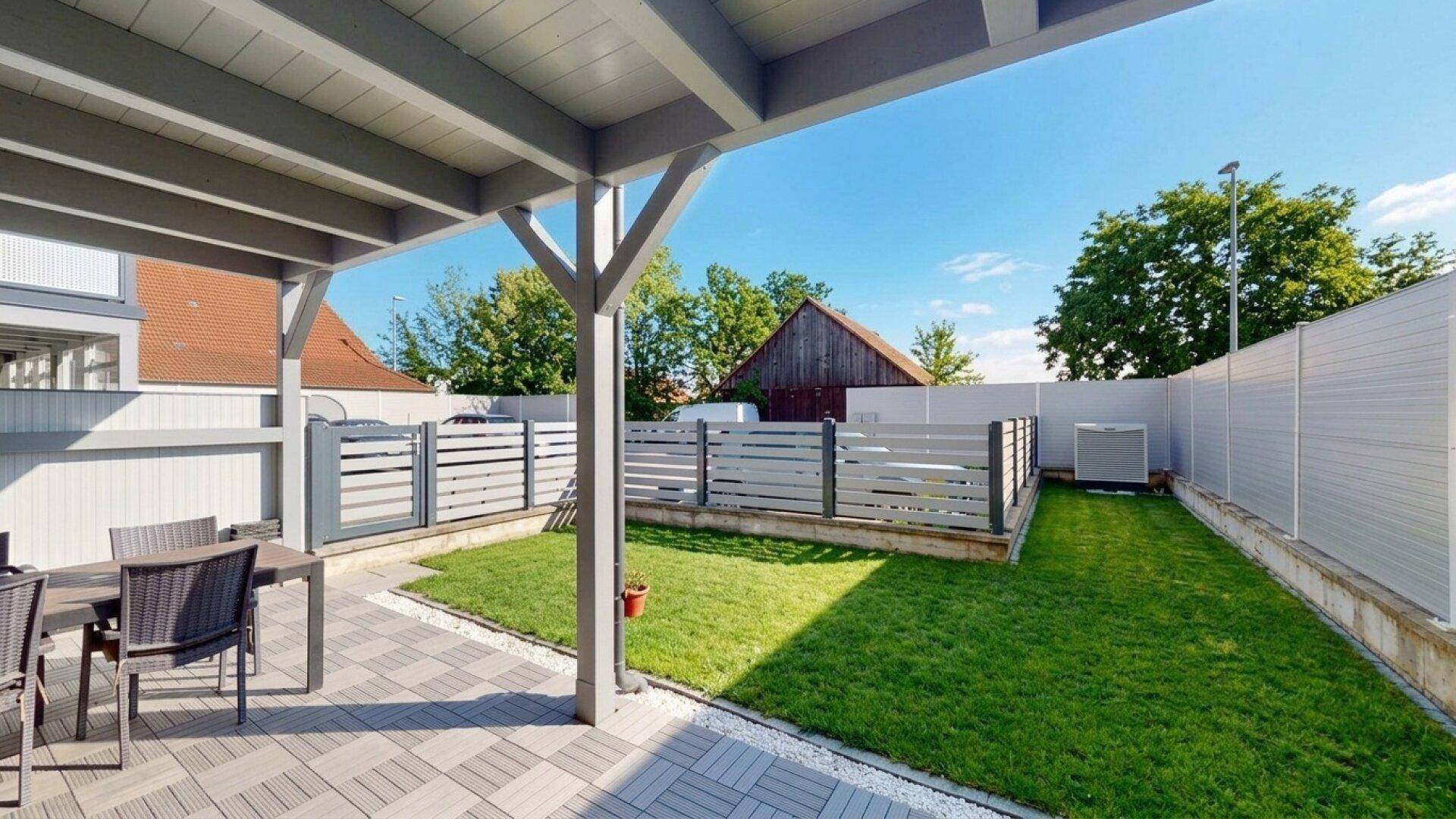 Überdachte Terrasse mit Sitzgelegenheiten und Blick auf den kleinen, gepflegten Garten.