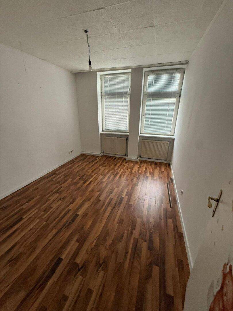 Kleineres Zimmer mit Laminatboden und zwei Fenstern, ideal als Schlaf- oder Arbeitszimmer.
