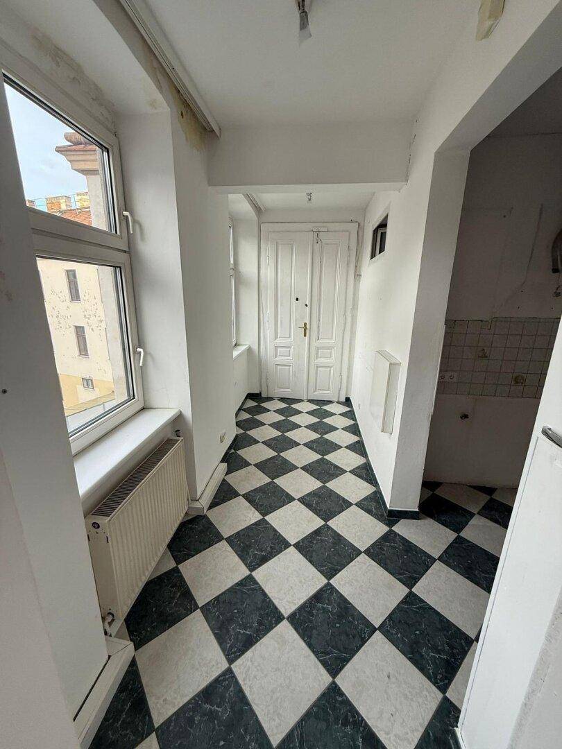 Flur mit markantem schwarz-weiß kariertem Fliesenboden und Fenster, das Tageslicht hereinlässt.