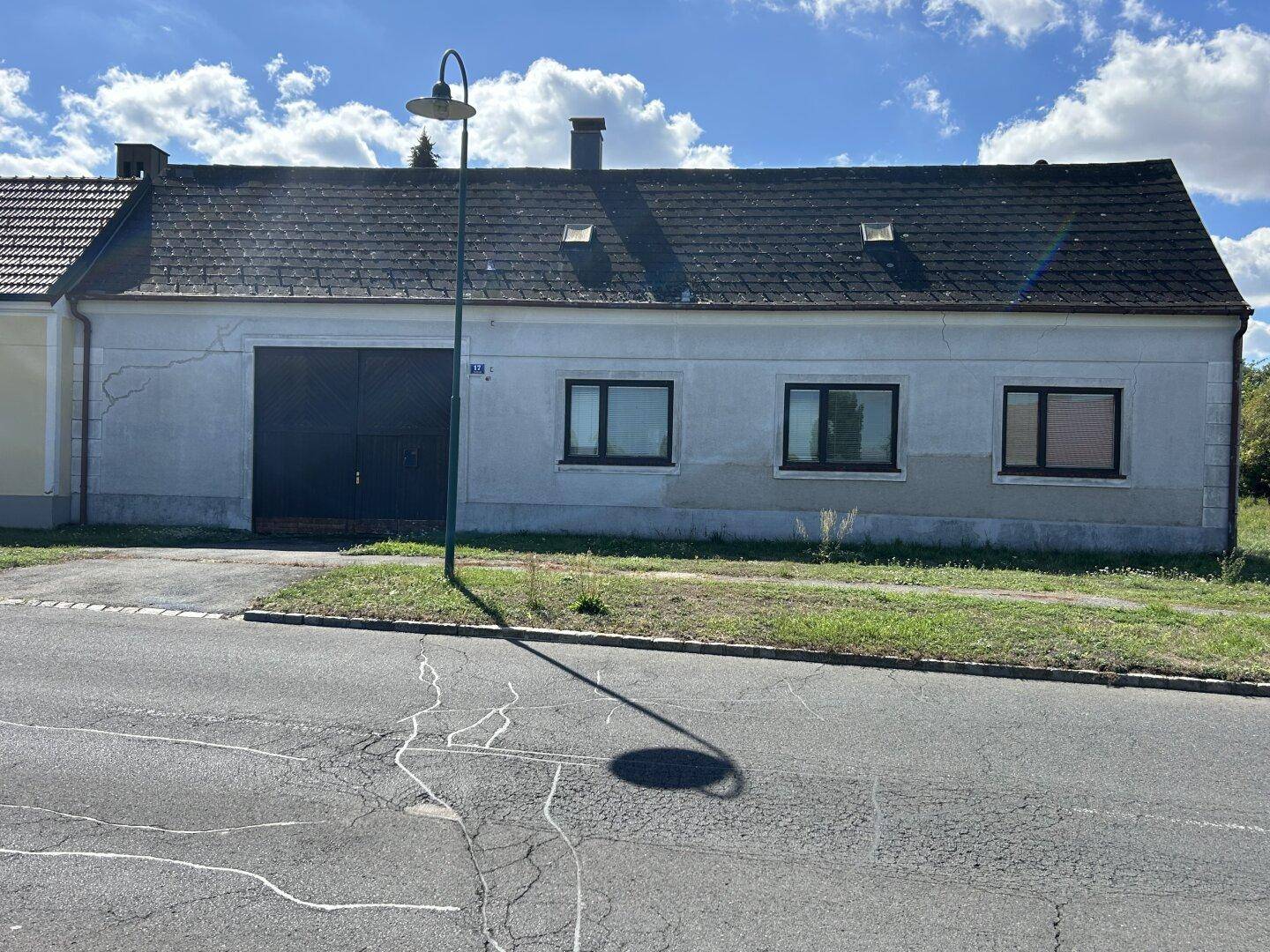Ländliches Haus mit grauer Fassade und großem Garagentor direkt an einer Straße gelegen.