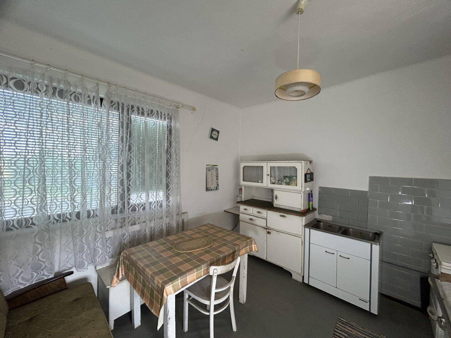 Einfache Wohnküche mit Esstisch, Spüle und Fenster mit Jalousien.