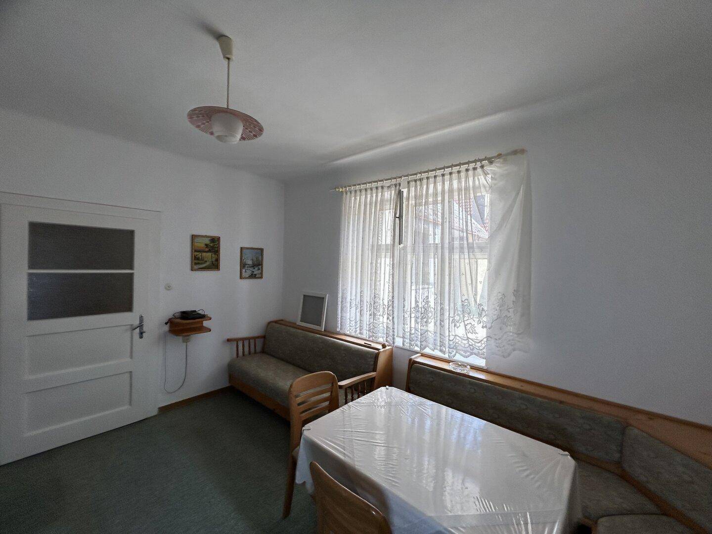 Gemütliches Wohnzimmer mit Esstisch, Eckbank und einem Fenster mit Vorhängen.