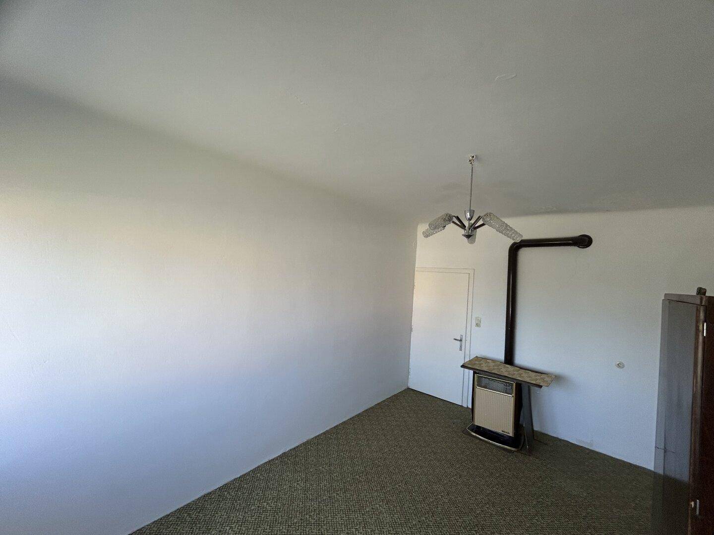 Leeres Schlafzimmer mit Teppichboden und einem Holzofen als Heizquelle.