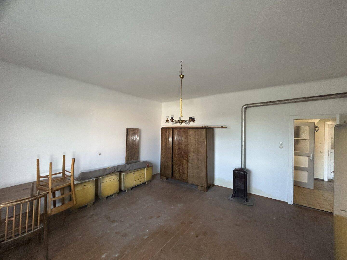 Geräumiges Wohnzimmer mit Holzboden, einem Holzofen und verschiedenen Möbelstücken.
