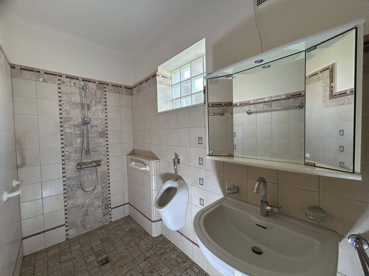 Badezimmer mit Fliesenboden, Waschbecken, Urinal und Spiegelschrank.