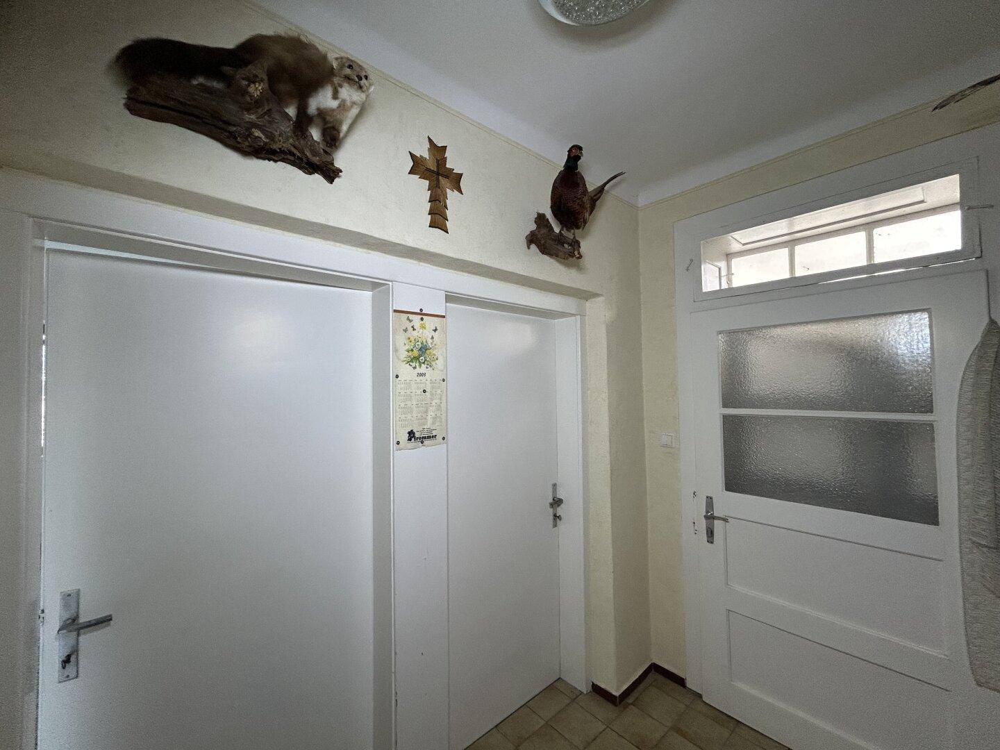 Flur mit zwei weißen Türen, Fliesenboden und rustikaler Dekoration an der Decke.