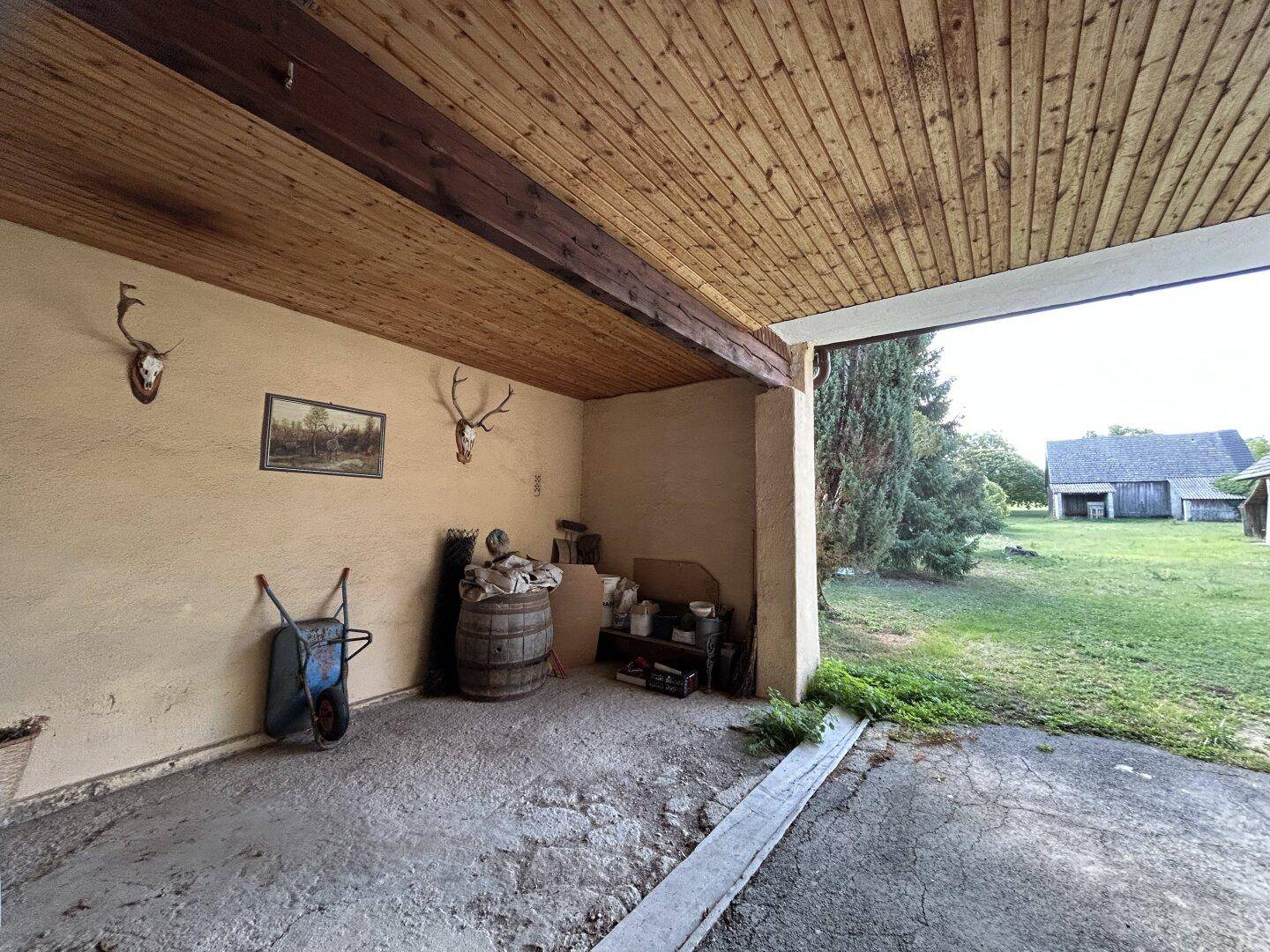 Überdachter Außenbereich mit rustikaler Holzdecke und Jagdtrophäen, Blick ins Grüne.