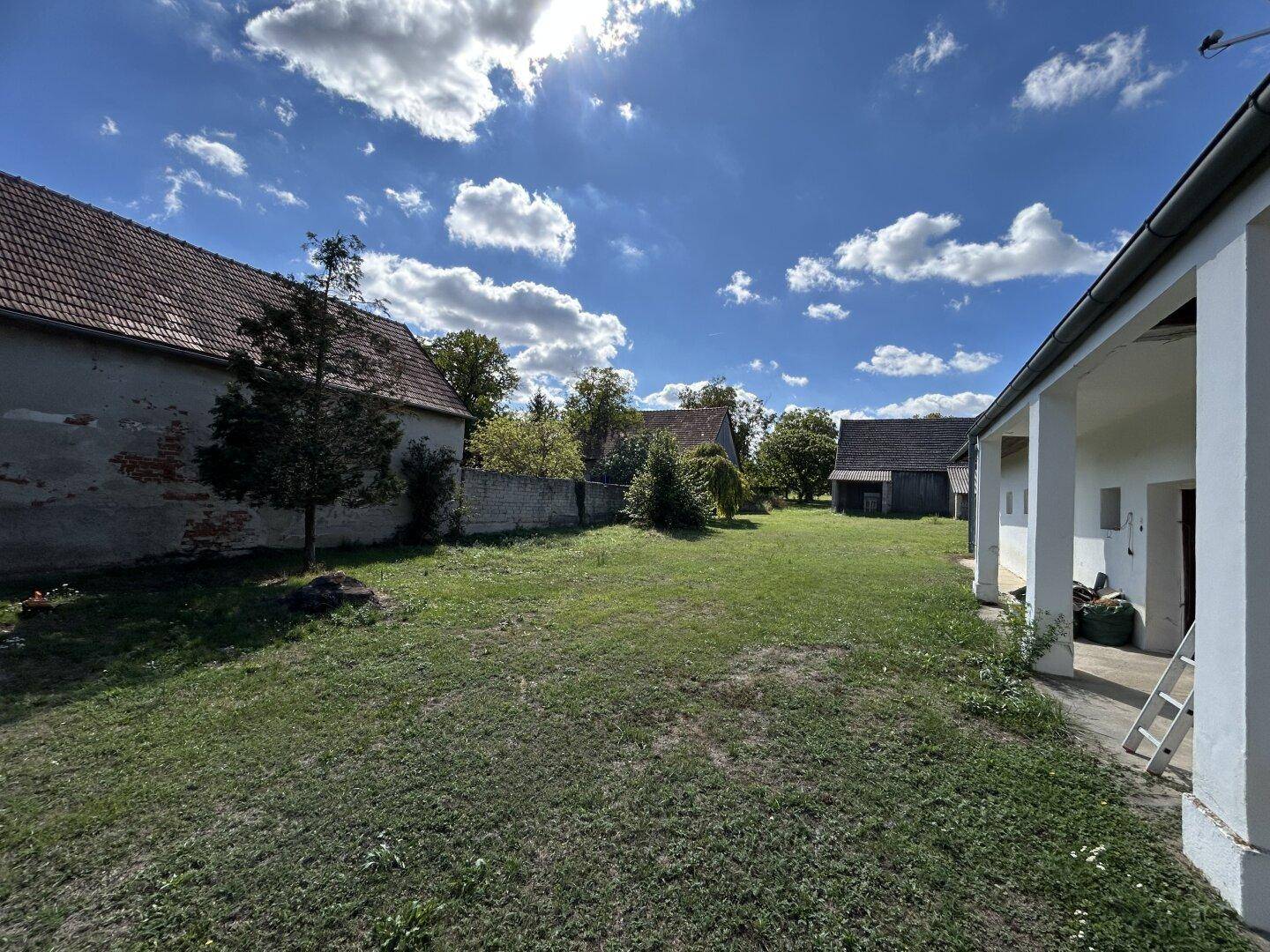 Weitläufiger grüner Bereich mit Blick auf mehrere ländliche Gebäude unter einem sonnigen Himmel.