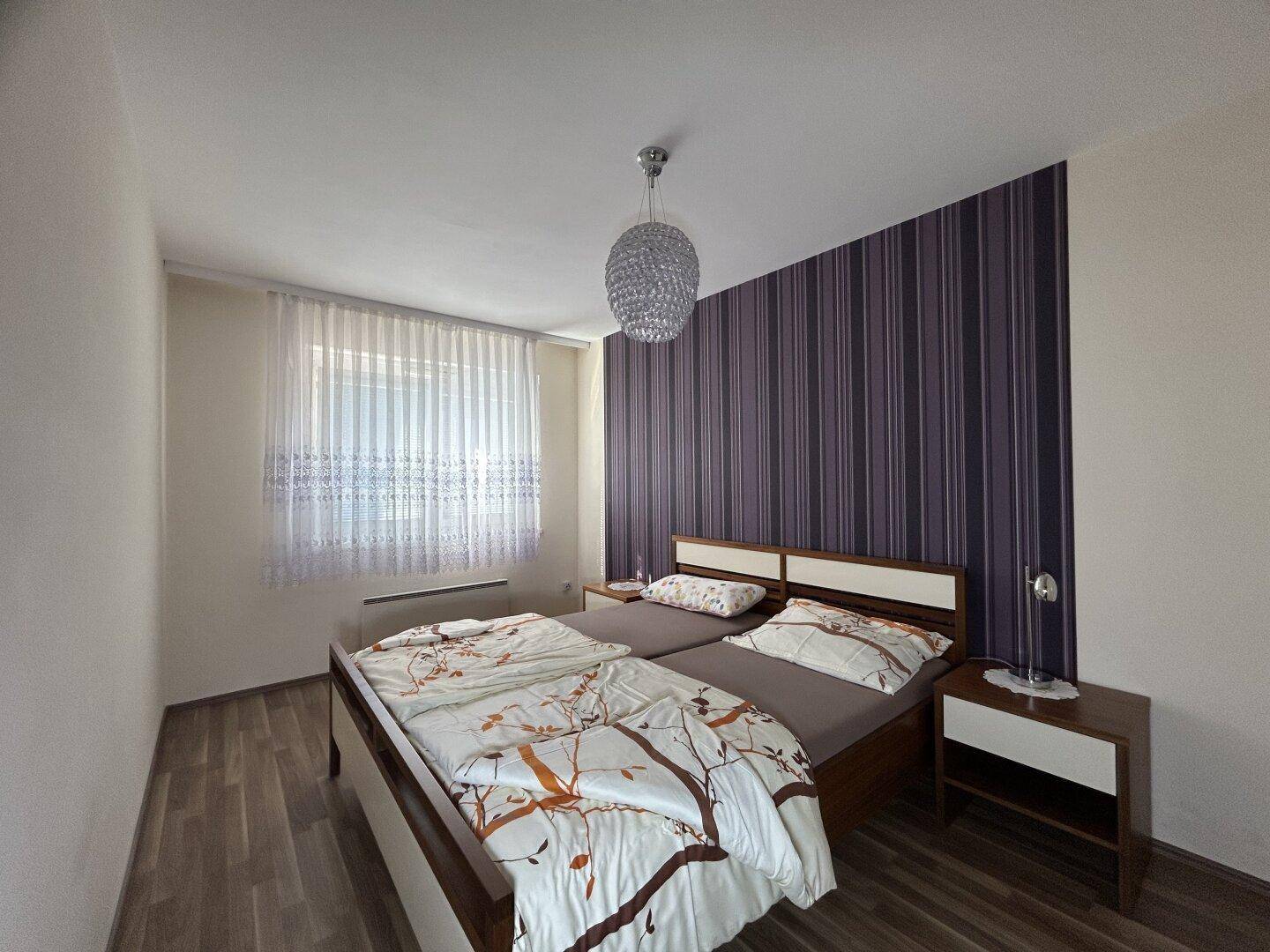 Schlafzimmer mit Doppelbett, gestreifter Akzentwand und Parkettboden, bietet eine gemütliche Atmosphäre.