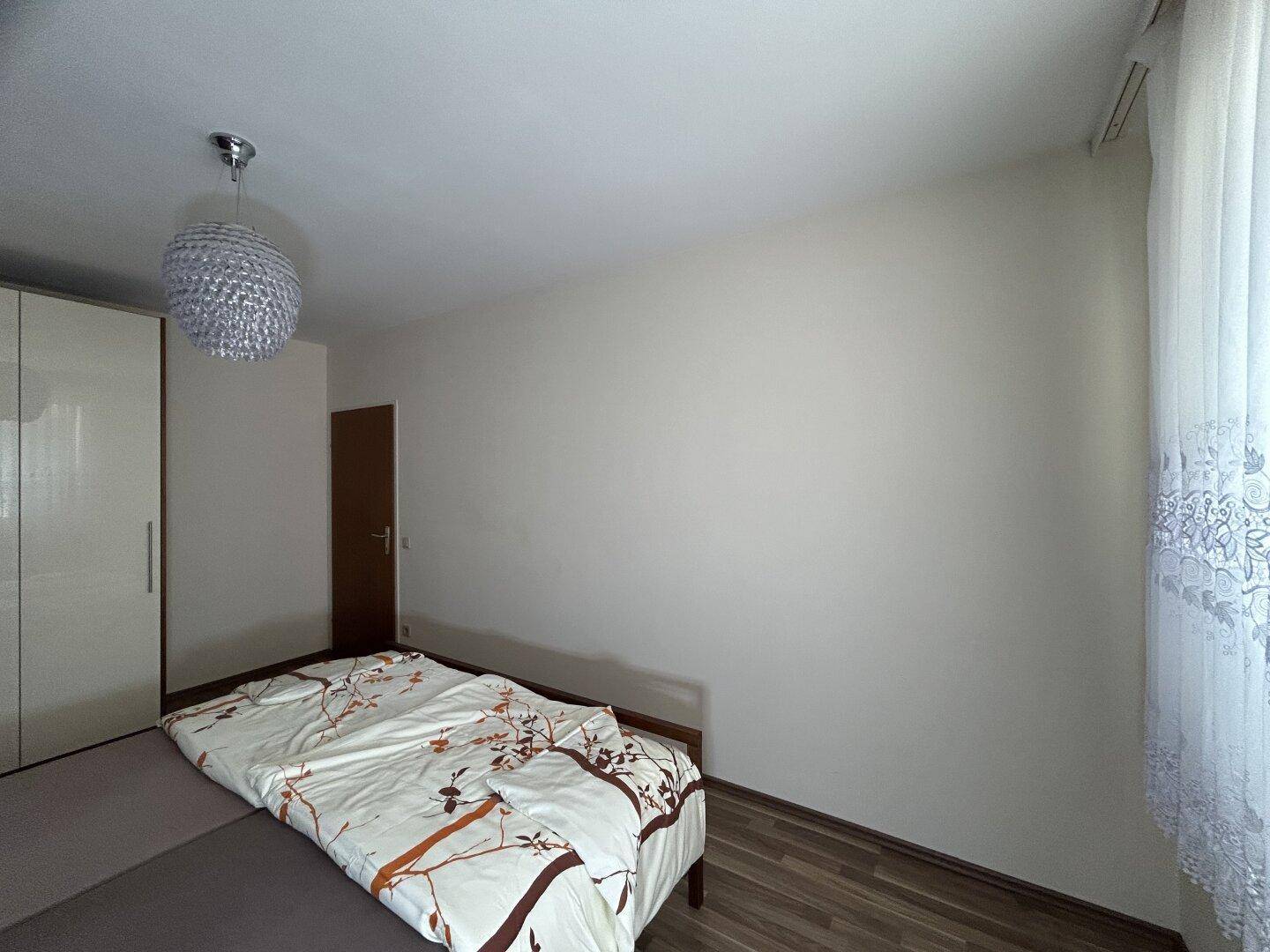 Helles Schlafzimmer mit Doppelbett und Fenster, bietet viel Tageslicht und eine ruhige Umgebung.