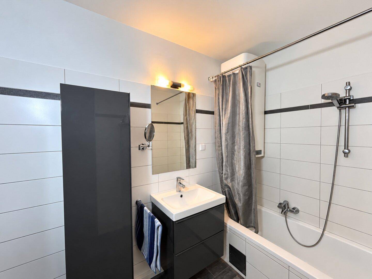 Modernes Badezimmer mit Badewanne, Waschtisch und Spiegel, in hellen Fliesen gehalten.