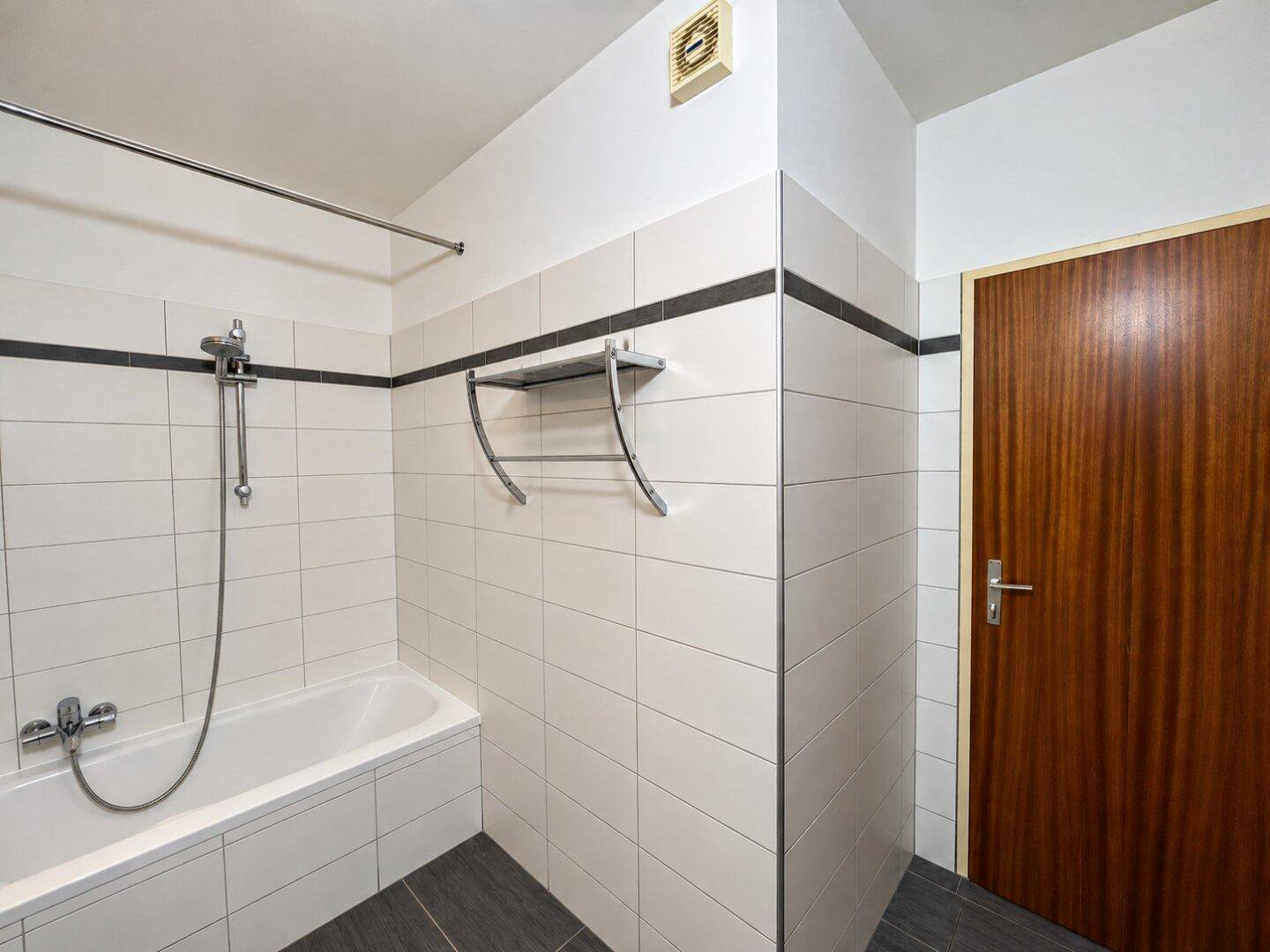 Badezimmer mit Badewanne und Duschvorrichtung, schlicht und funktional gestaltet.