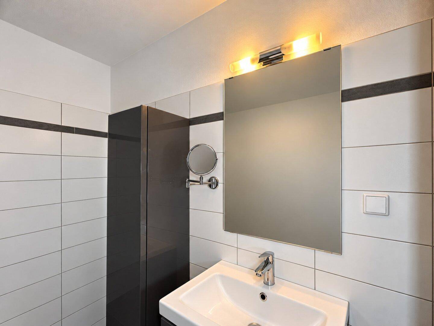Badezimmer mit modernem Waschtisch, Spiegel und integriertem Schrank, bietet Stauraum.