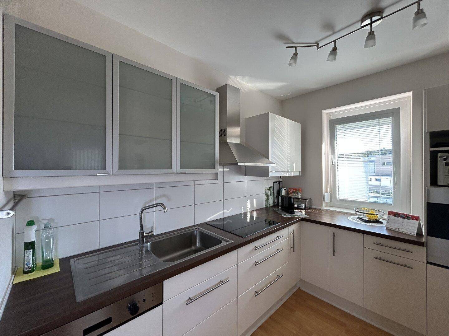 Moderne Küche mit weißen Schränken, Edelstahlspüle und Fenster, gut ausgestattet für den Alltag.