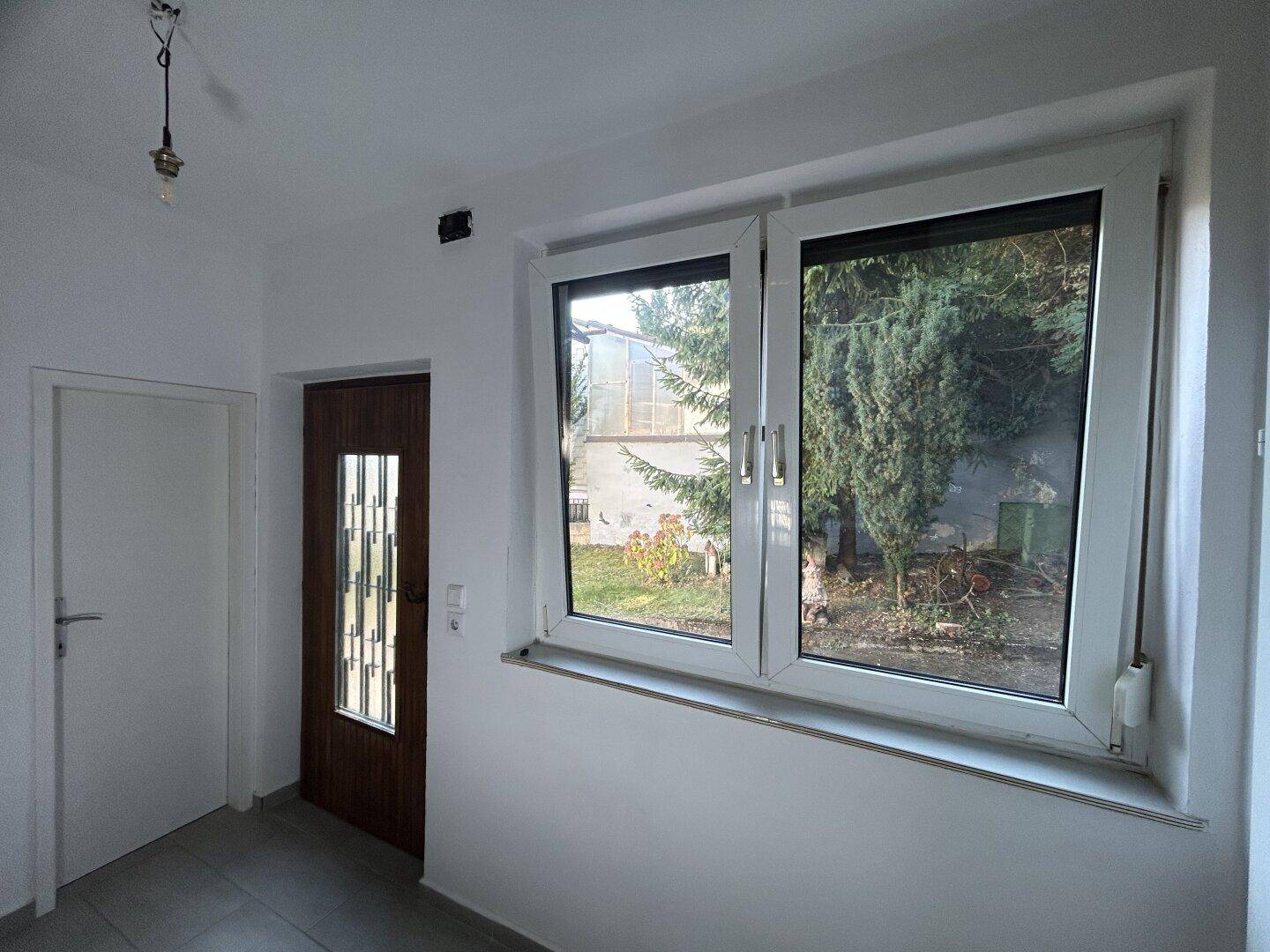 Eingangsbereich mit Fliesenboden, Holztür und Blick in den Garten durch große Fenster.