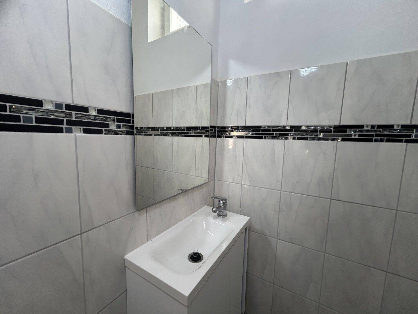 Kleines Badezimmer mit modernen Fliesen, Einzelwaschbecken und Spiegel über dem Waschtisch.