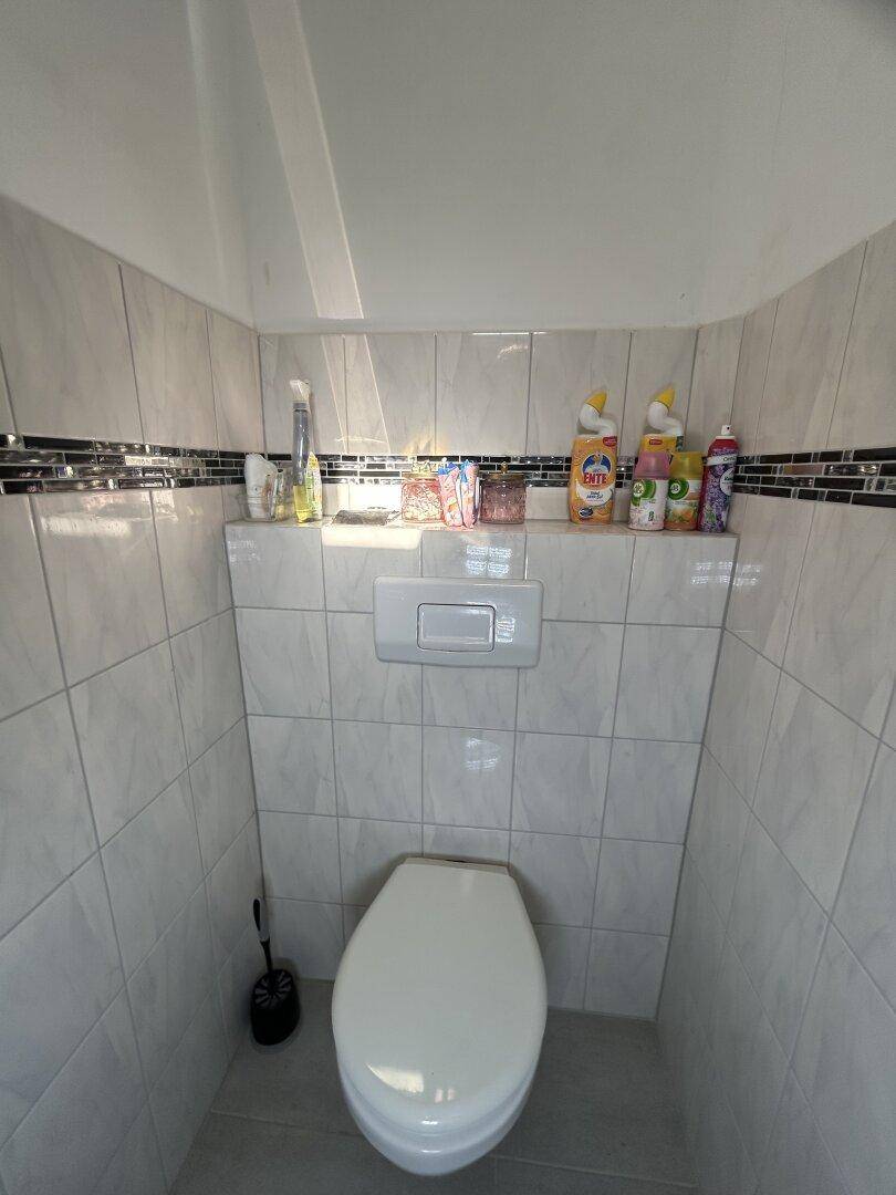 WC-Bereich mit modernen Fliesen, Wand-WC und Ablagefläche für Utensilien.