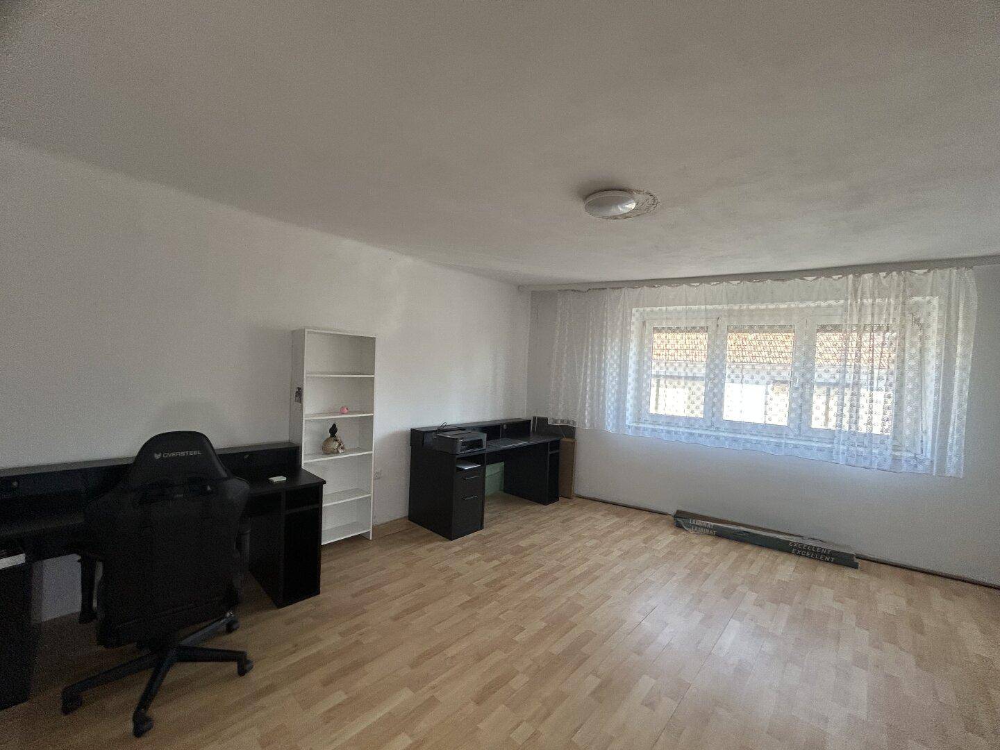 Geräumiges Zimmer mit Laminatboden, großem Fenster und Schreibtischbereich.