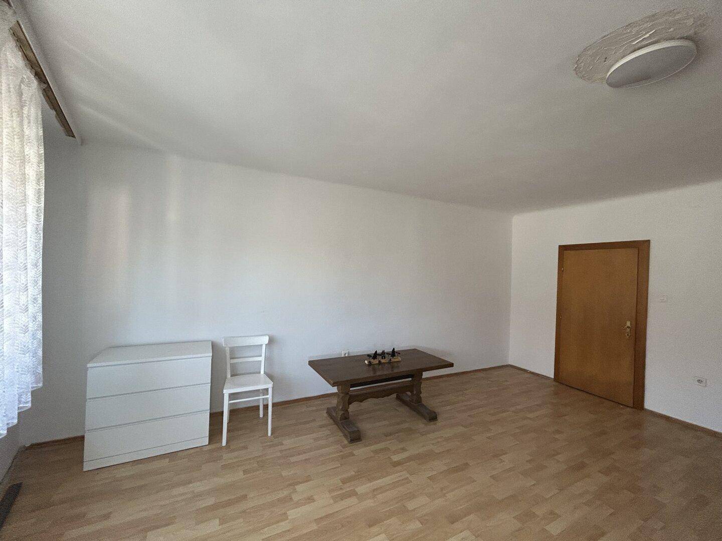 Helles Zimmer mit Laminatboden, weiß gestrichenen Wänden und Holztür.