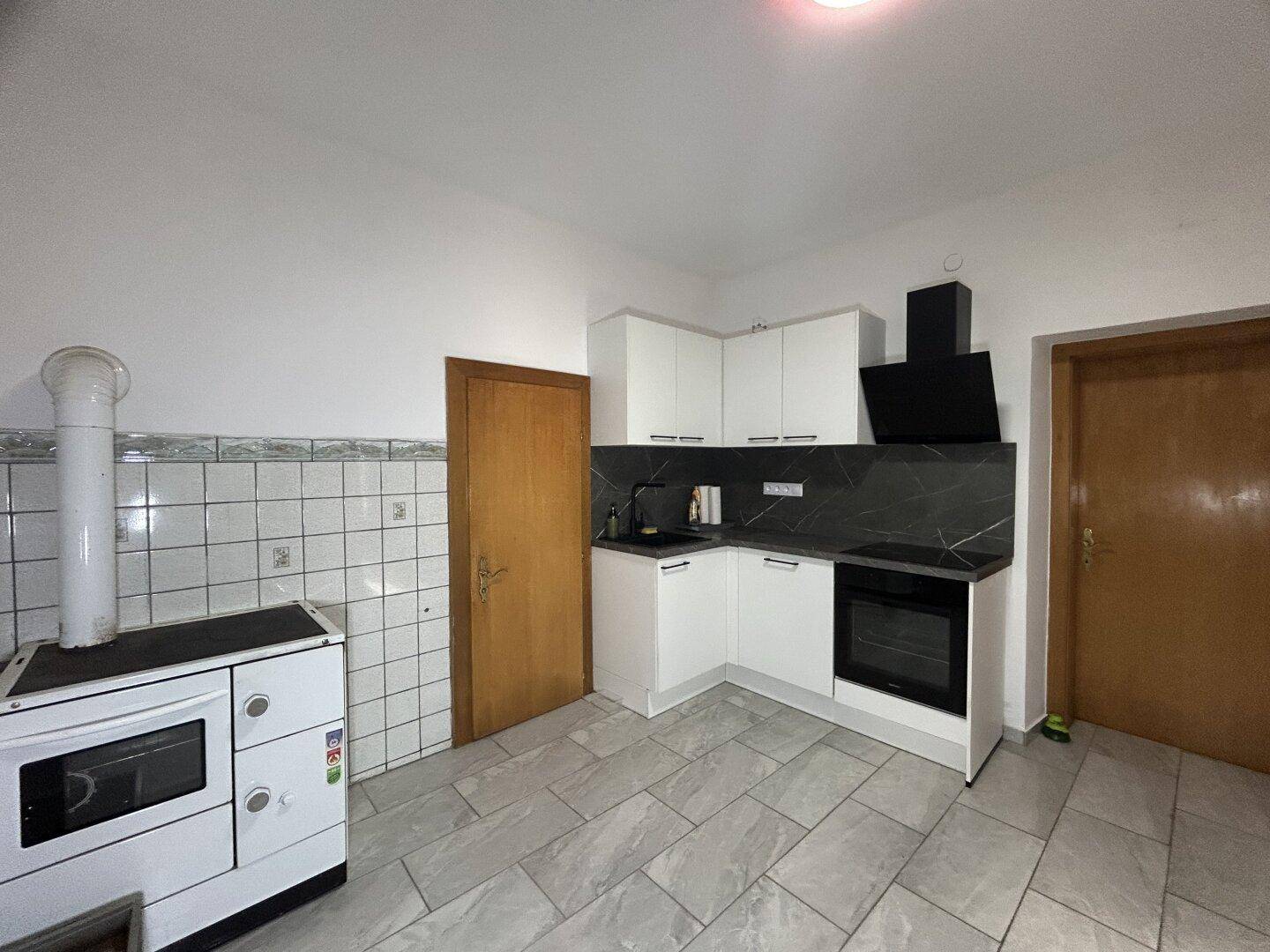 Moderne Küche mit weißen Schränken, dunkler Arbeitsplatte und traditionellem Holzofen.