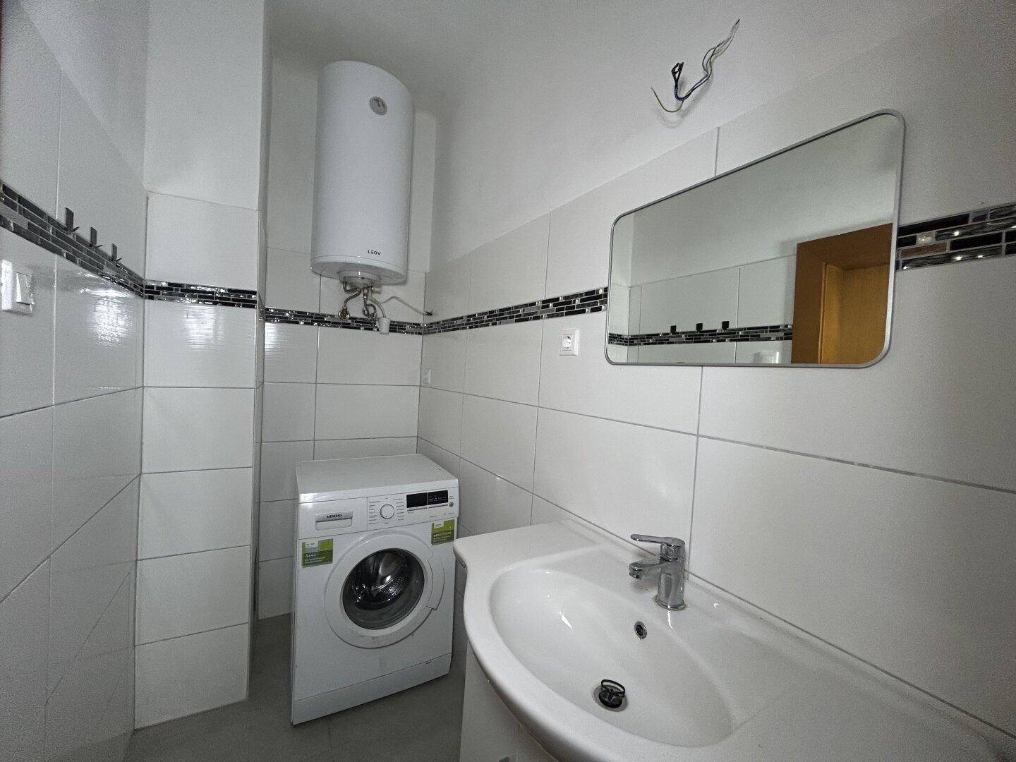 Modernes Badezimmer mit Fliesen, Waschbecken, Waschmaschine und Warmwasserboiler.