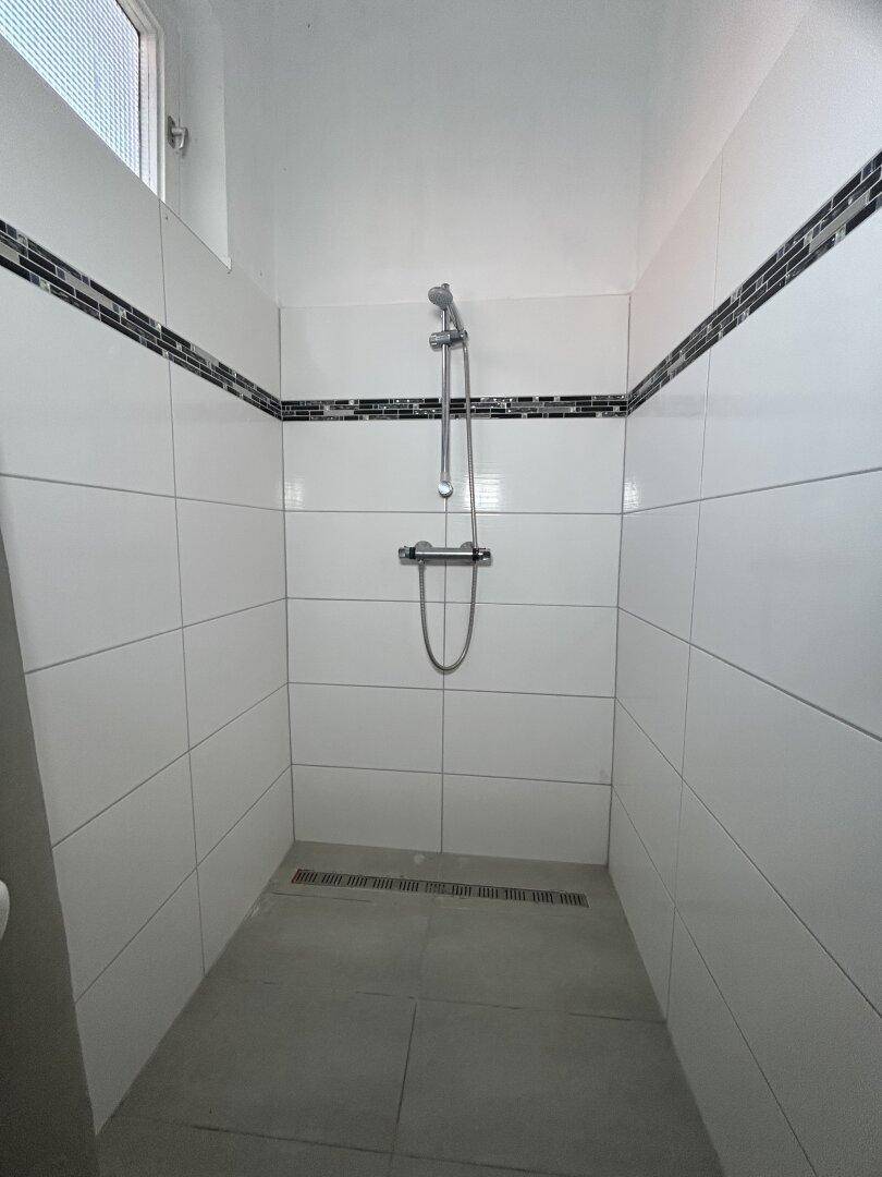 Geräumige Dusche mit modernen Fliesen, Duschkopf und Fenster für Tageslicht.