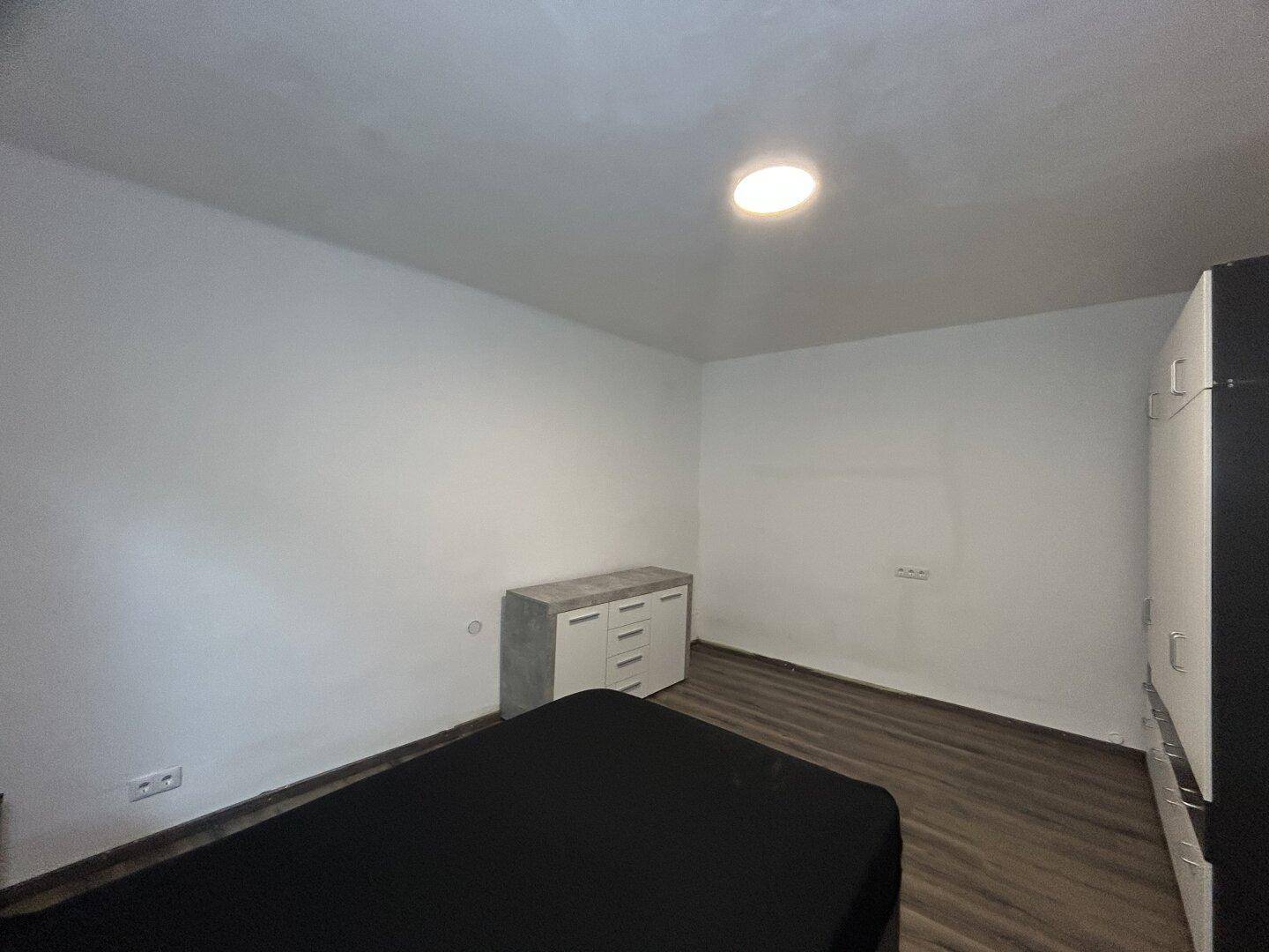 Schlafzimmer mit modernem Bett, Kommode und Laminatboden.