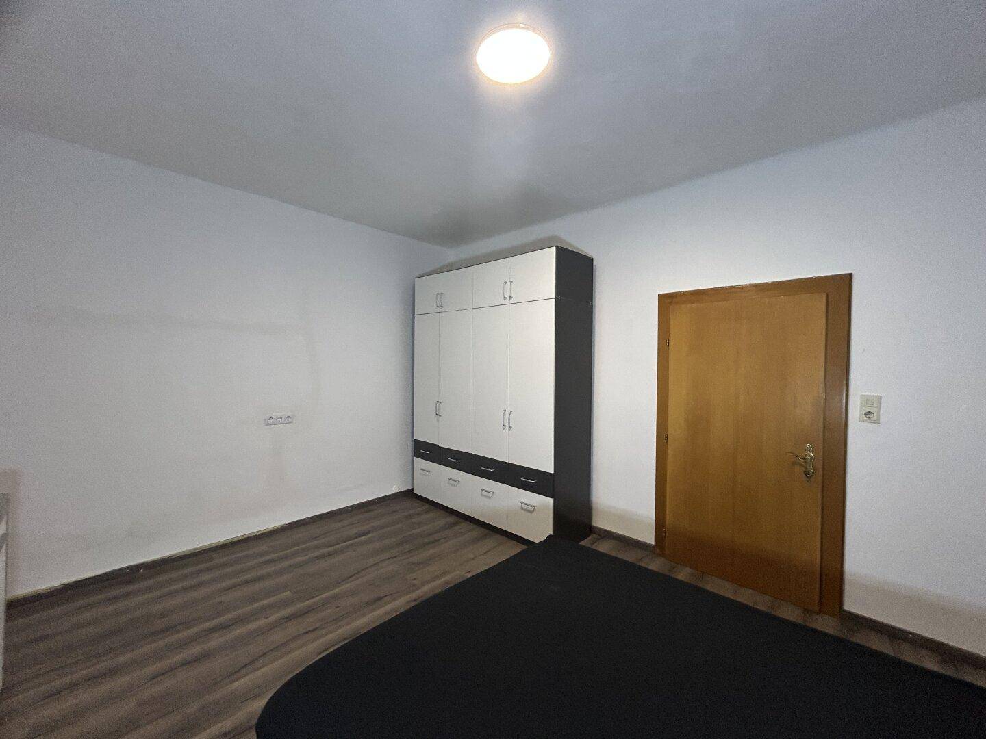 Schlafzimmer mit Laminatboden, großem Kleiderschrank und Holztür.