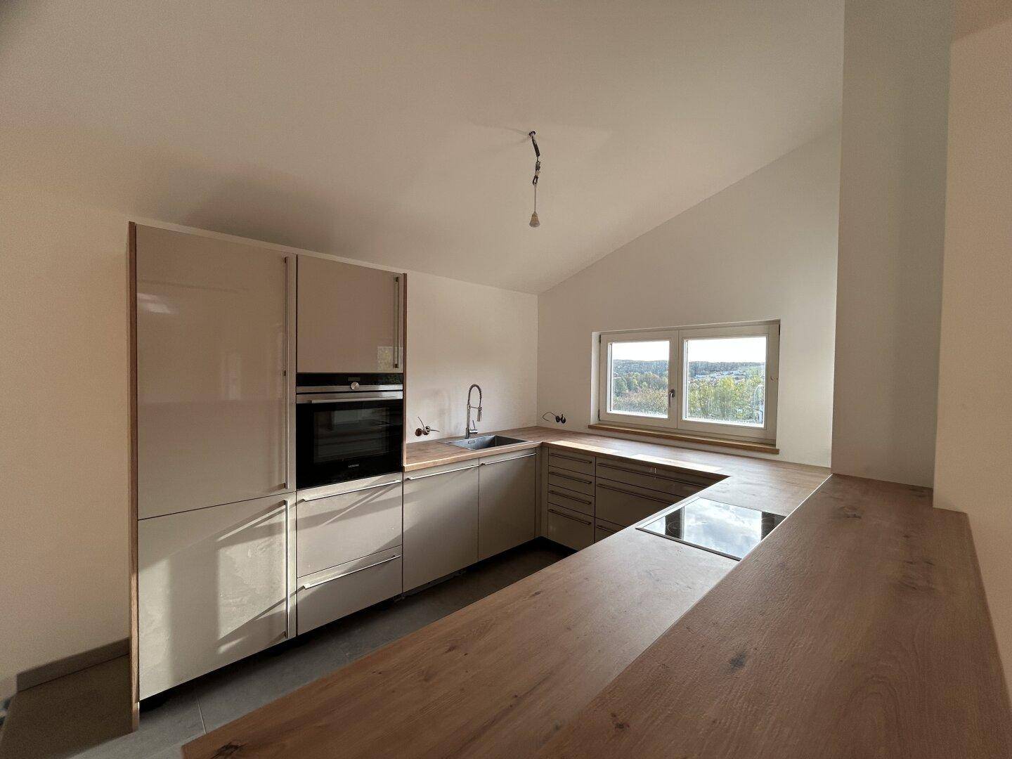 Geräumige Küche mit modernen Einbauschränken, Holz-Arbeitsplatten und Kochfeld mit Aussicht.