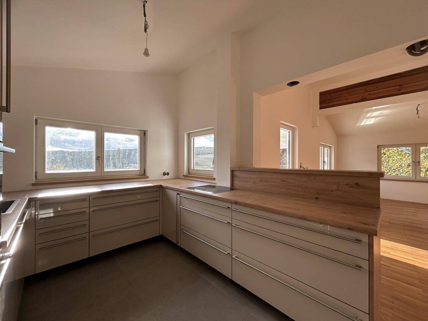 Moderne Küche mit Holz-Arbeitsplatten, hellen Schränken und offenem Übergang zum Wohnbereich.